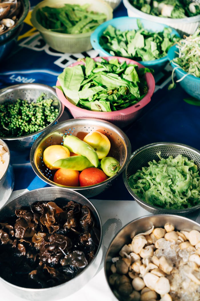 An array of vibrant vegetables and greens displayed in colorful colanders and bowls.