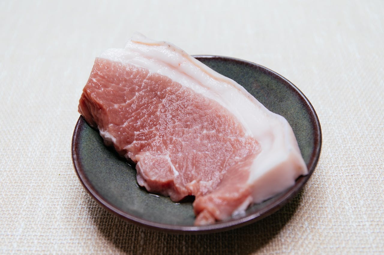 Close-up of a raw pork slice on a dark plate, ideal for culinary themes.