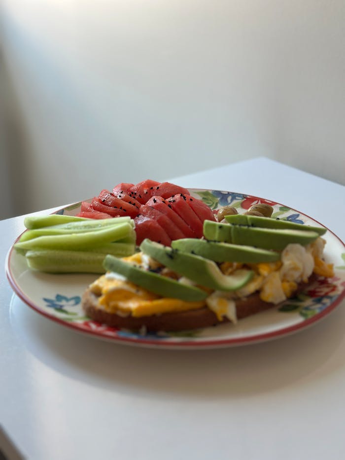 Plate of avocado toast with eggs, watermelon, and cucumber slices, perfect for a nutritious breakfast.