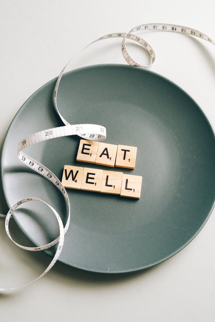 Creative photo of 'Eat Well' letter tiles on a plate with measuring tape, symbolizing balanced nutrition.